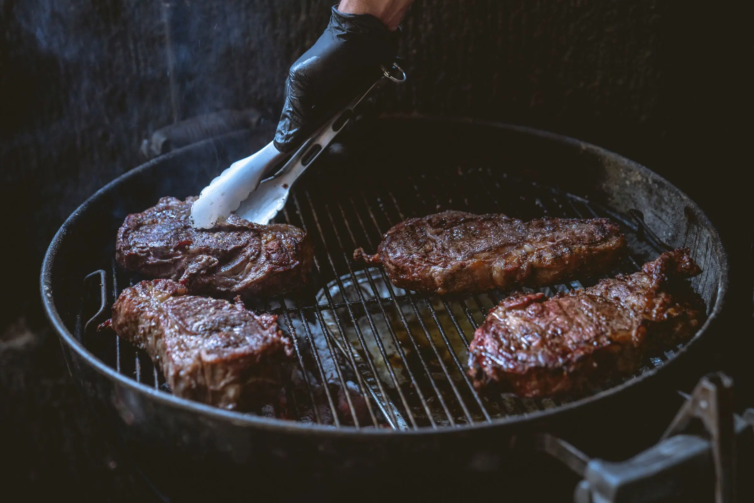El parrillero girando piezas de carne sobre la parrilla de carbón